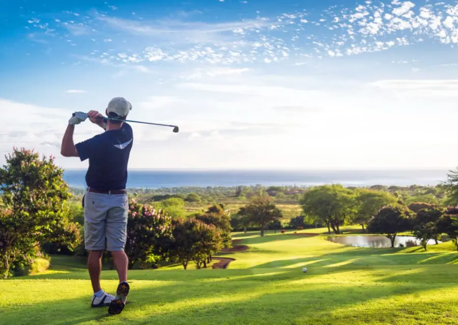 A golfer follows through on a drive above a green course with the ocean beyond