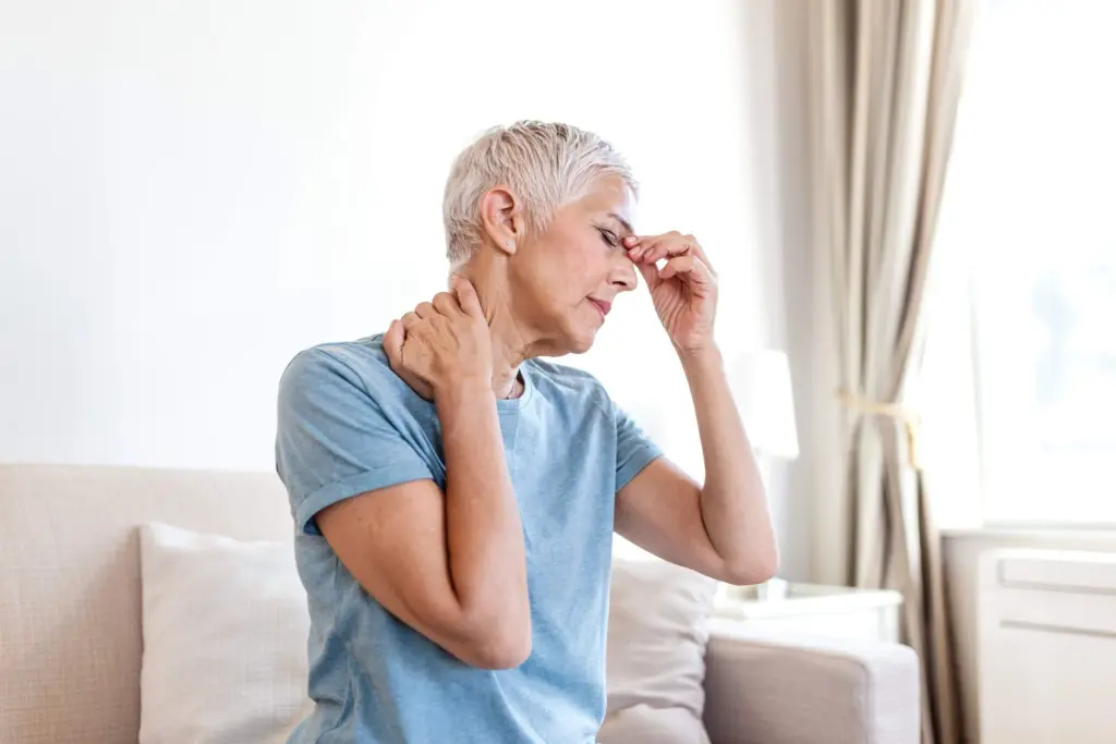 A woman pressing her fingers to her neck and forehead in discomfort