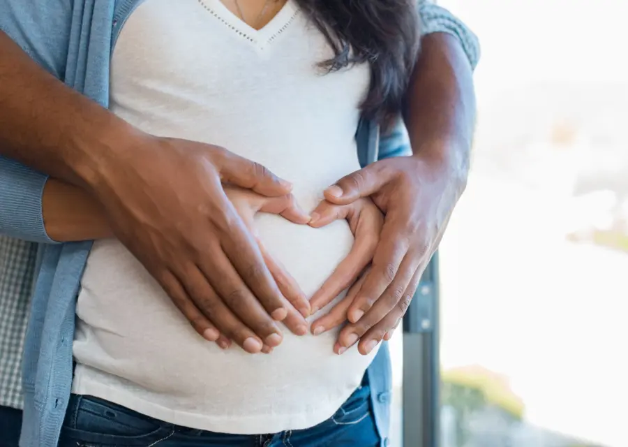 An expectant mother cradling her belly with her partner's hands